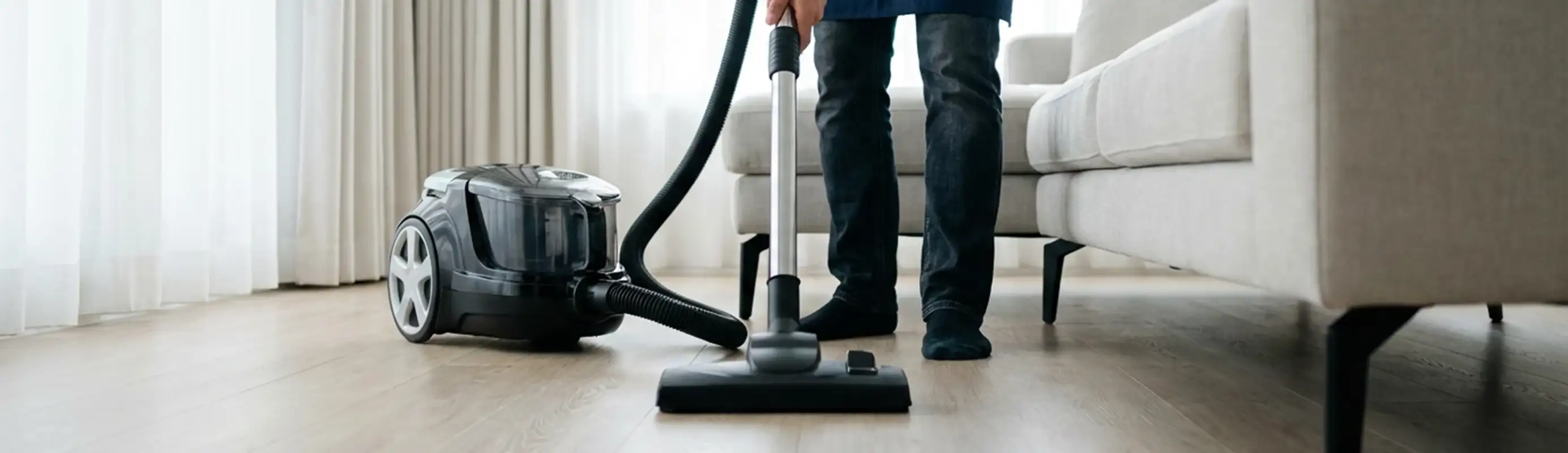 Professional house cleaner vacuuming a living room floor with a canister vacuum cleaner, Tacoma, WA.