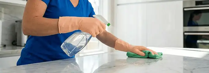 Maid service worker spraying and wiping a kitchen countertop with a microfiber cloth for sanitizing, Tacoma, WA.