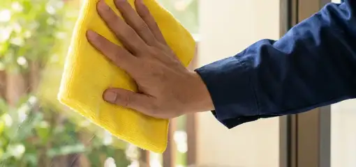 House cleaner wiping a glass window with a yellow microfiber cloth for streak-free cleaning, Tacoma, WA.